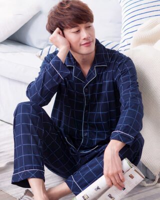 Men's casual navy blue checkered cotton pajamas worn by a man sitting on a rug in front of a bed in a house