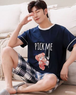 Summer pajamas t-shirt blue night bear pattern and plaid shorts worn by a man sitting on a carpet in a house