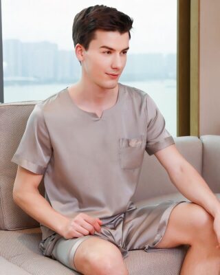 Grey satin pajamas for men worn by a man sitting on a sofa in a house