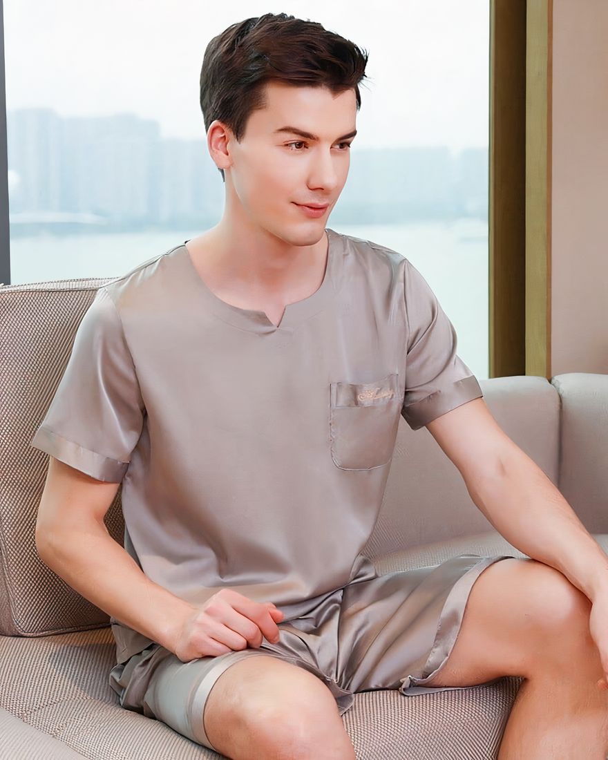 Grey satin pajamas for men worn by a man sitting on a sofa in a house