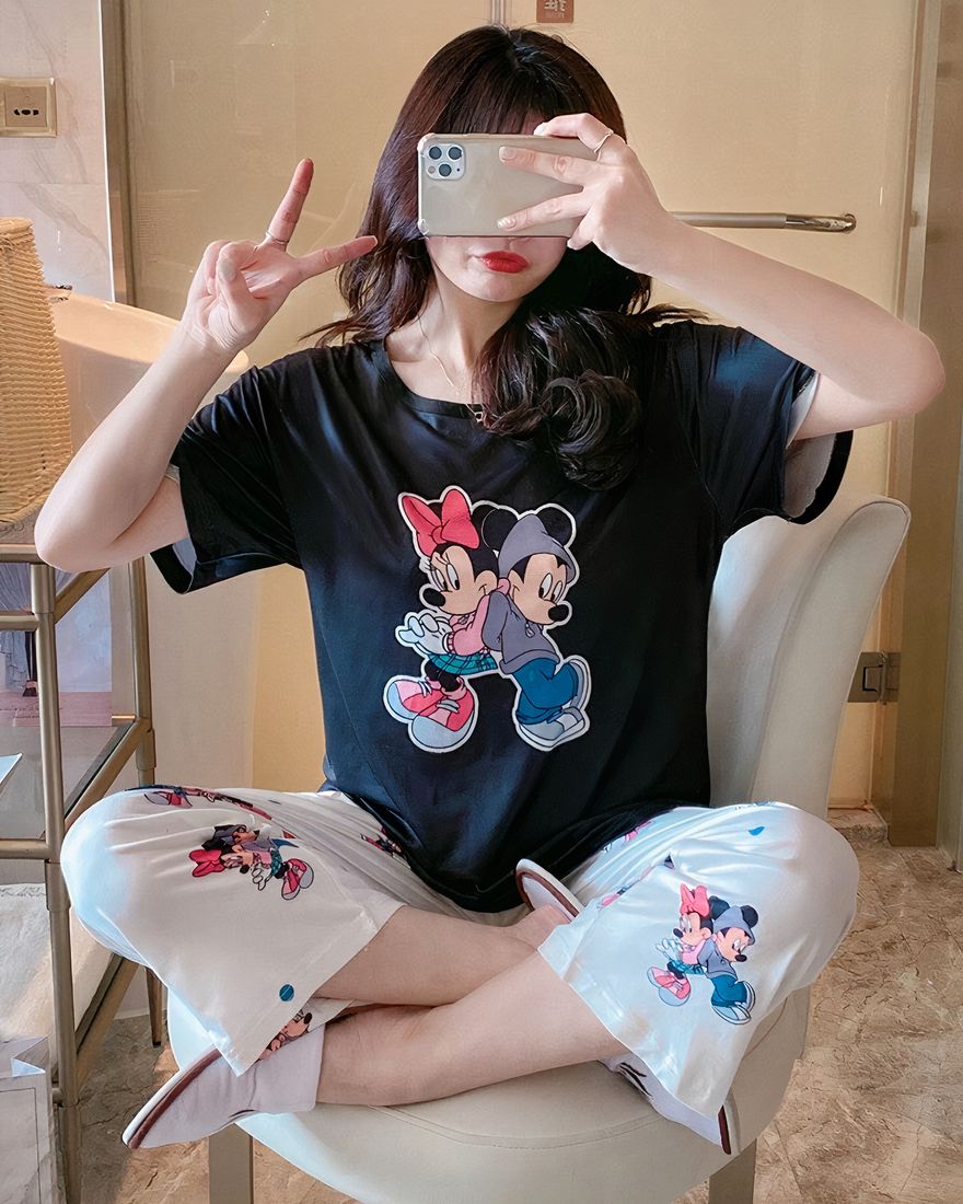 Black two-piece pajamas with Minnie and Mickey pattern worn by a woman sitting on a fashionable chair in a house