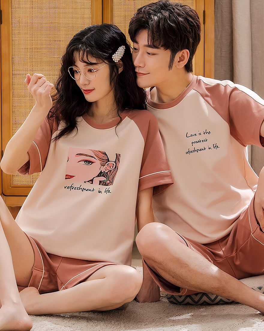 Two-piece cotton pajamas with white and pink shorts worn by a couple sitting on a carpet in a house