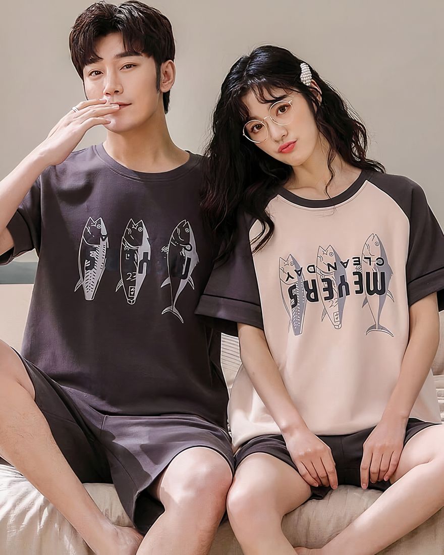 Two-piece cotton pajamas with fish print worn by a couple sitting on a bed in a house