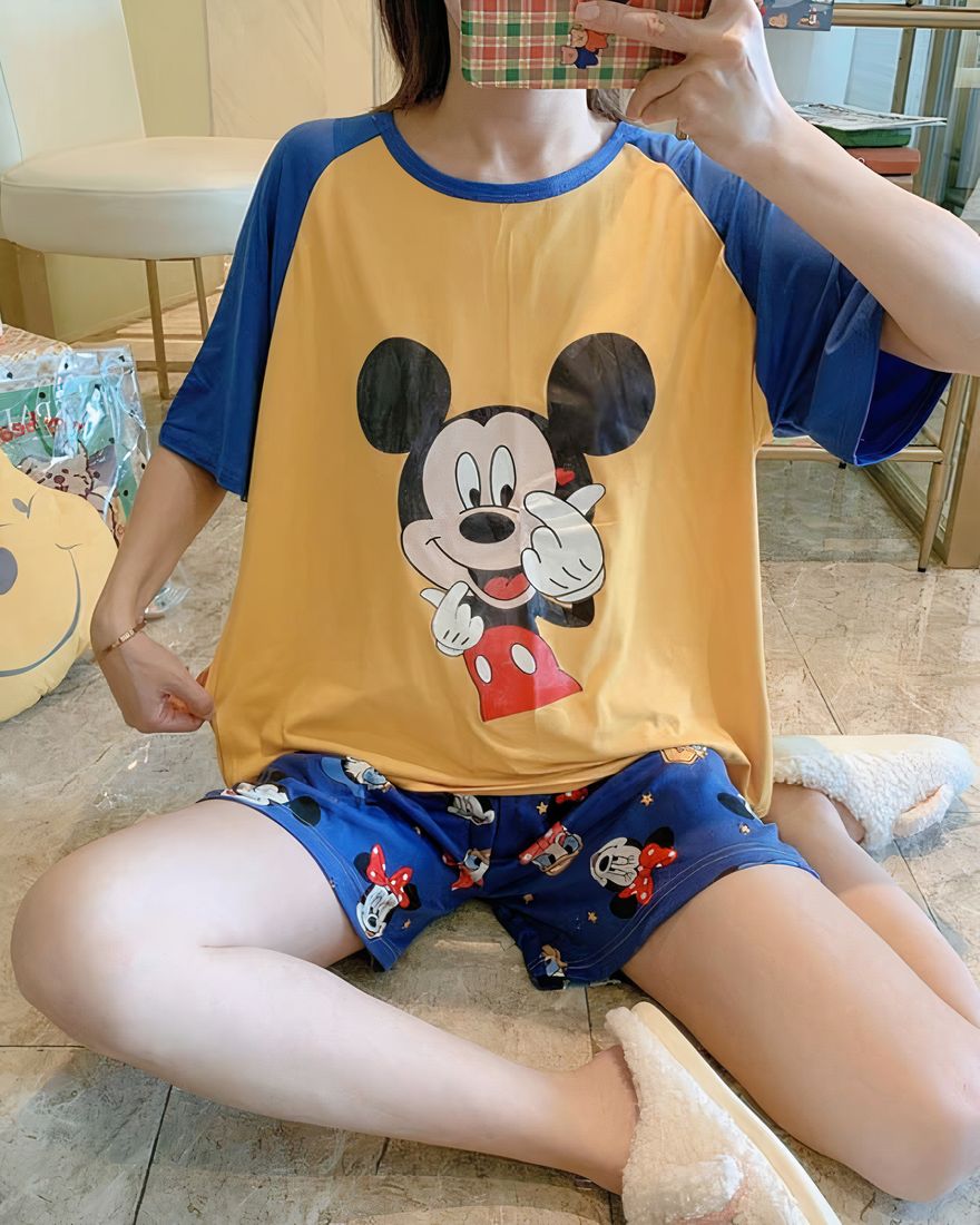 Two-piece pyjamas t-shirt and shorts with Mickey motif worn by a woman sitting on who is taking a picture in a house