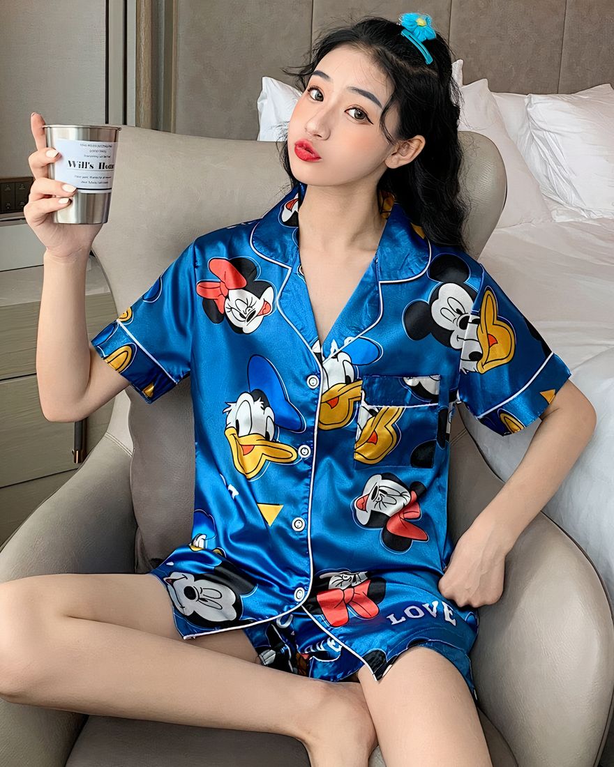 Two-piece satin pajamas with Mickey, Minnie and Donald blue pattern worn by a woman sitting on a chair in a house