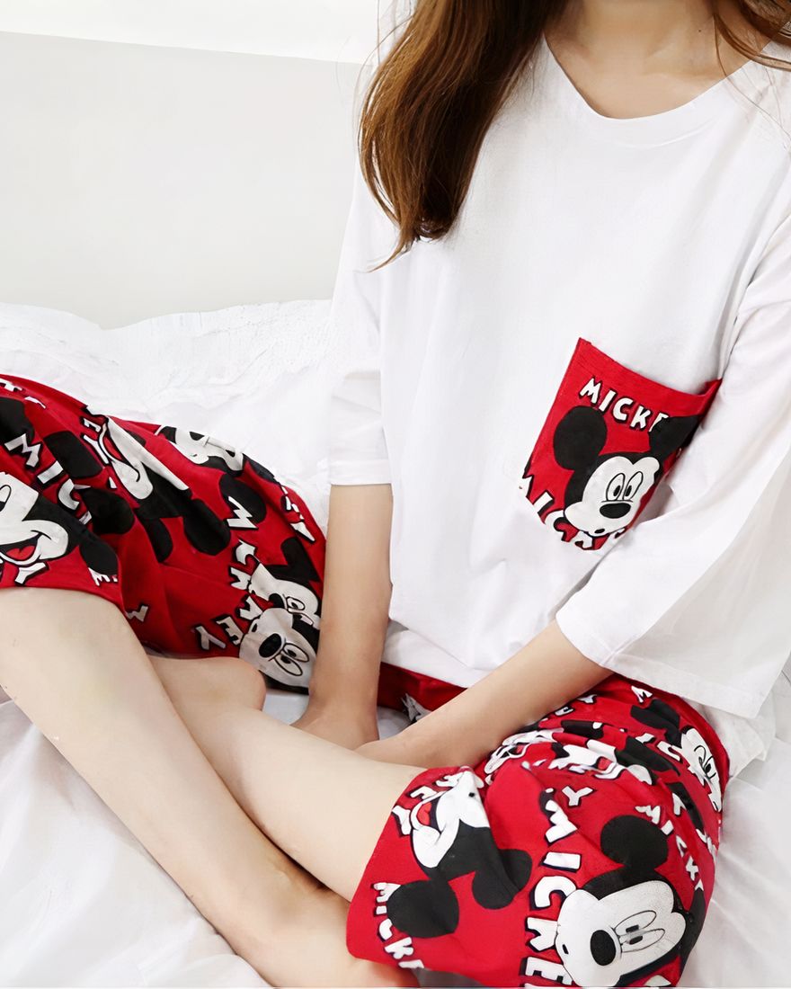 Red and white two-piece pyjamas with a Mickey motif worn by a woman sitting on a bed in fashion