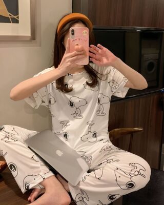 Two-piece short-sleeved pajamas with a dog motif worn by a seated woman taking a picture in a house