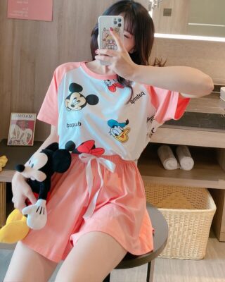 Pink Mickey and Donald print summer pajamas worn by a woman sitting on a chair taking a phoo in a house