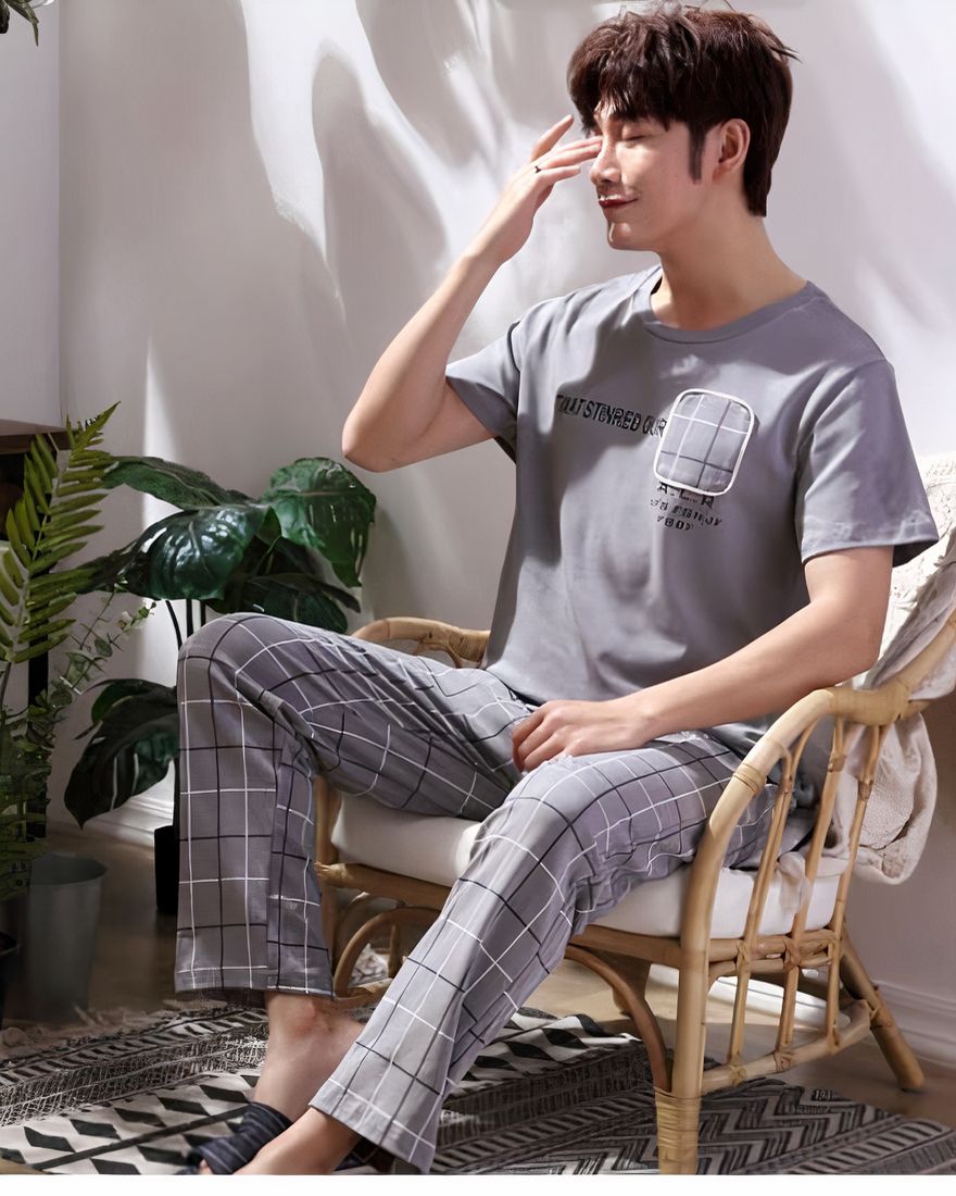 Short sleeved plaid pajamas for men worn by a man sitting on a chair in a house