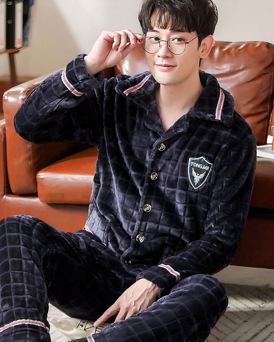 Men's flannel pajamas with check pattern worn by a man sitting on a carpet in front of a sofa in a house