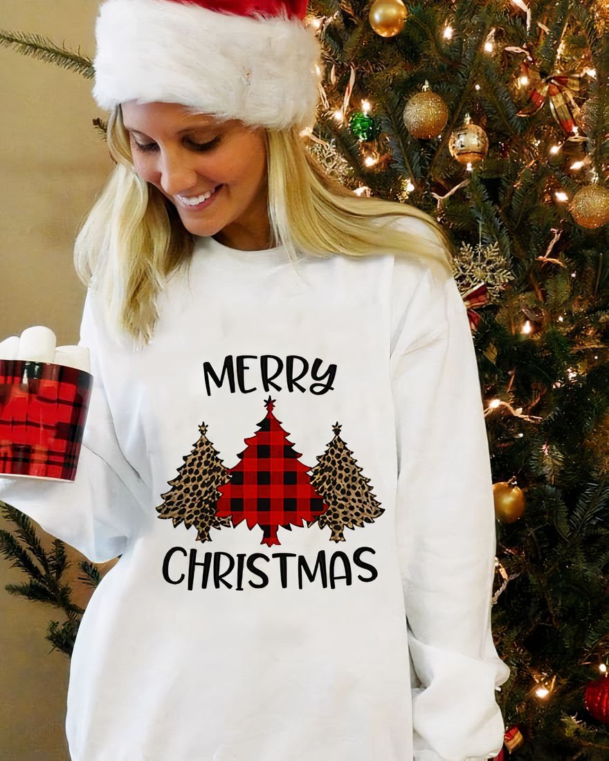 Women's long sleeve sweater with Christmas tree design and "Merry Christmas" worn by a woman in front of a Christmas tree in a house