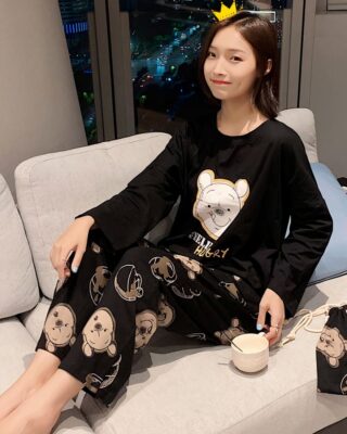 Black pajama set with Winnie the Pooh for fashionable women worn by a woman sitting on a sofa in a house