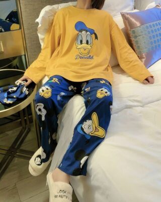 Cute Disney Donald pajamas for women in mustard yellow and blue worn by a woman sitting on a bed in a house