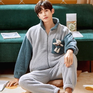 Winter pajamas with teddy bear for men worn by a man who sits on a carpet in front of a sofa in a house