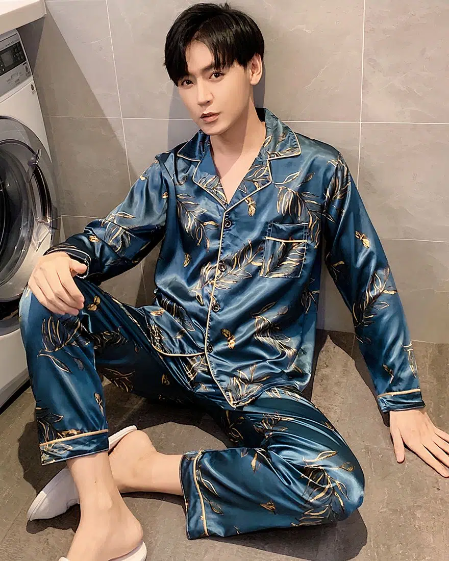 Men's satin blue pajamas worn by a man sitting in front of a washing machine in a house