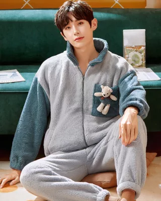 Winter pajamas with teddy bear for men worn by a man who sits on a carpet in front of a sofa in a house