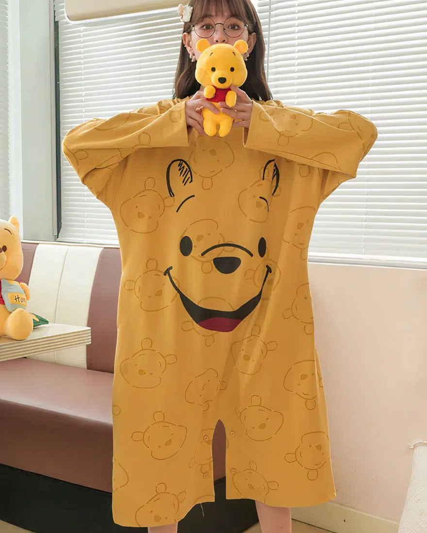 Mustard yellow Winnie the Pooh pajamas for women worn by a woman in front of a sofa in a house