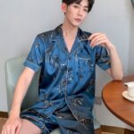 Blue silk summer pajamas for men worn by a man sitting on a chair in a house