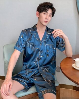 Blue silk summer pajamas for men worn by a man sitting on a chair in a house