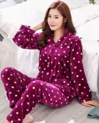 Elegant purple winter pajamas with small colored dots in white worn by a woman sitting on a carpet in front of a bed in a house