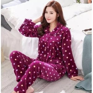 Elegant purple winter pajamas with small colored dots in white worn by a woman sitting on a carpet in front of a bed in a house