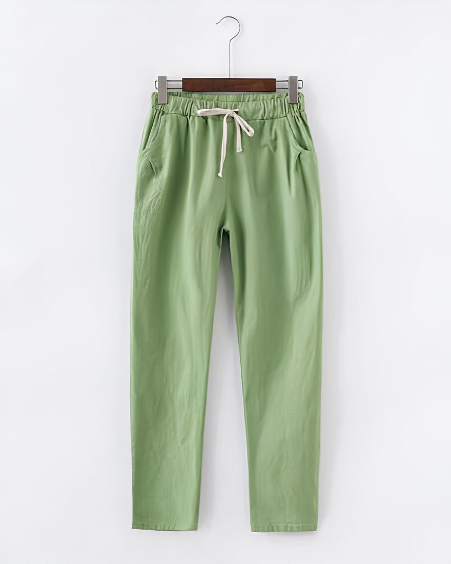 A pair of light green cotton and linen pants hanging on a hanger