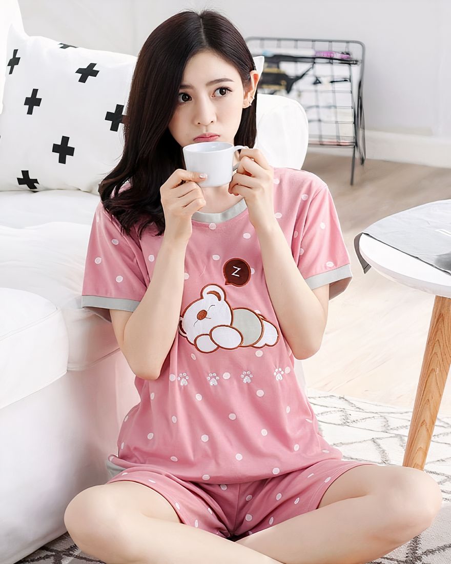 Pink short sleeve summer pajamas with sleeping bear pattern for women worn by a woman sitting on a rug in a house