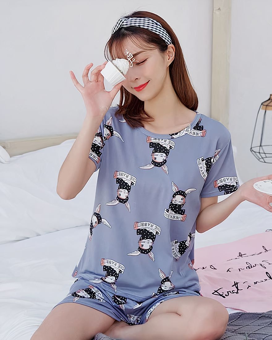 Summer pajamas with grey t-shirt and shorts for women with rabbit print worn by a woman sitting on a bed in a house