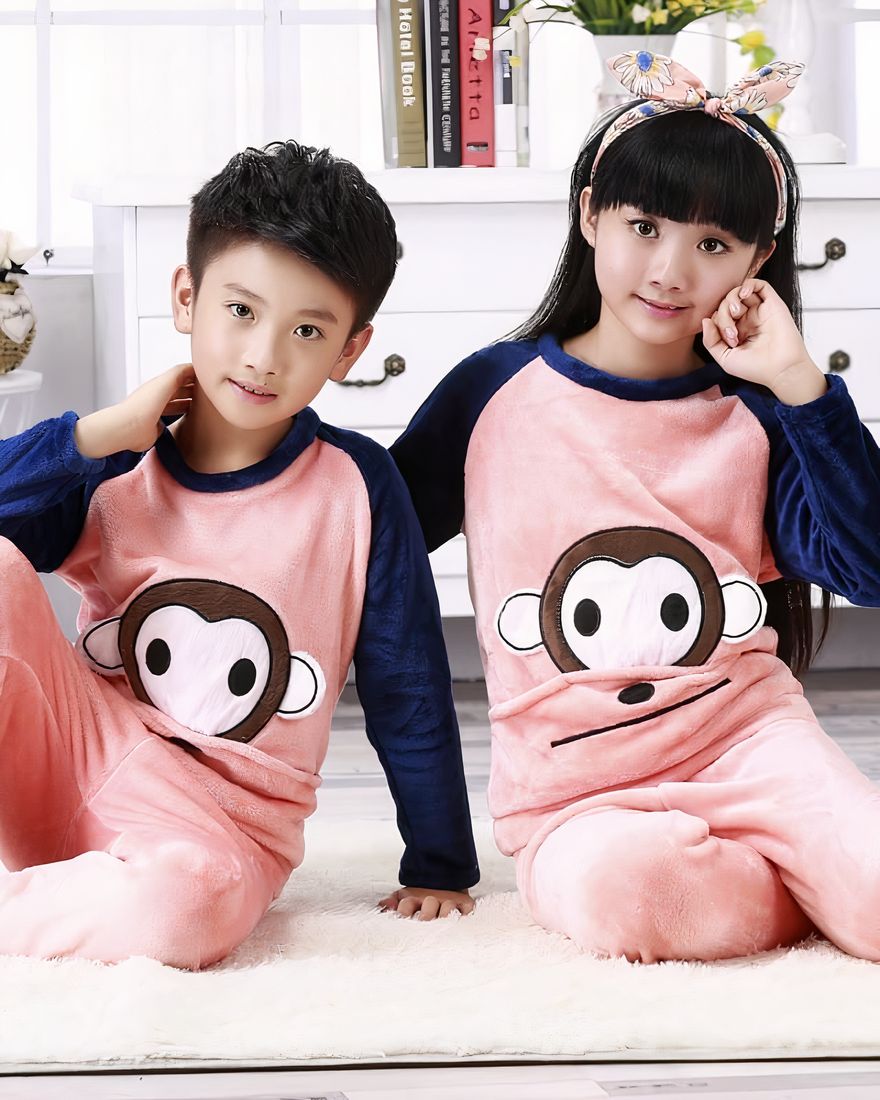 Flannel pajamas with monkey print for children worn by a little boy and a little girl sitting on a carpet in a house