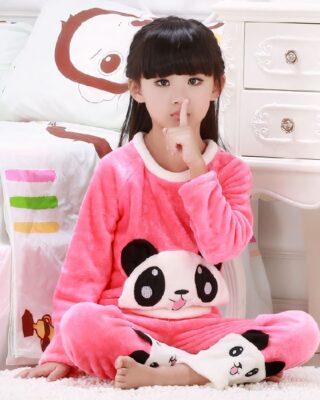 Pink two-piece panda pajamas for girl worn by a little girl sitting on a carpet in front of a bed in a house