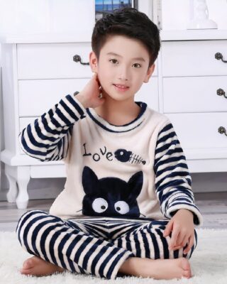 Two-piece black and white striped flannel pajamas for boy worn by a boy sitting on a carpet in a house