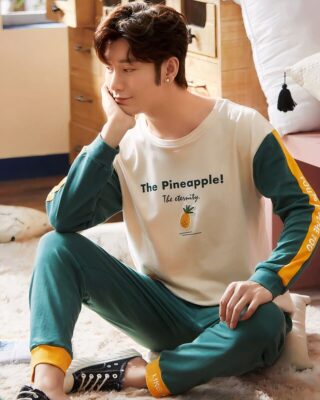 Pyjamas with white pineapple sweater and green pants worn by a man sitting on a carpet in a house