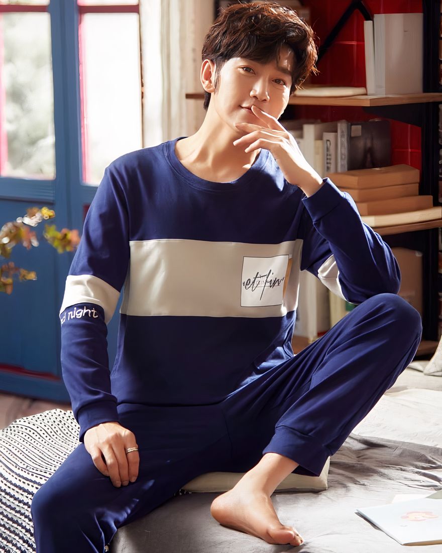Navy blue cotton two-piece long sleeve pajamas worn by a man sitting on a bed in a house