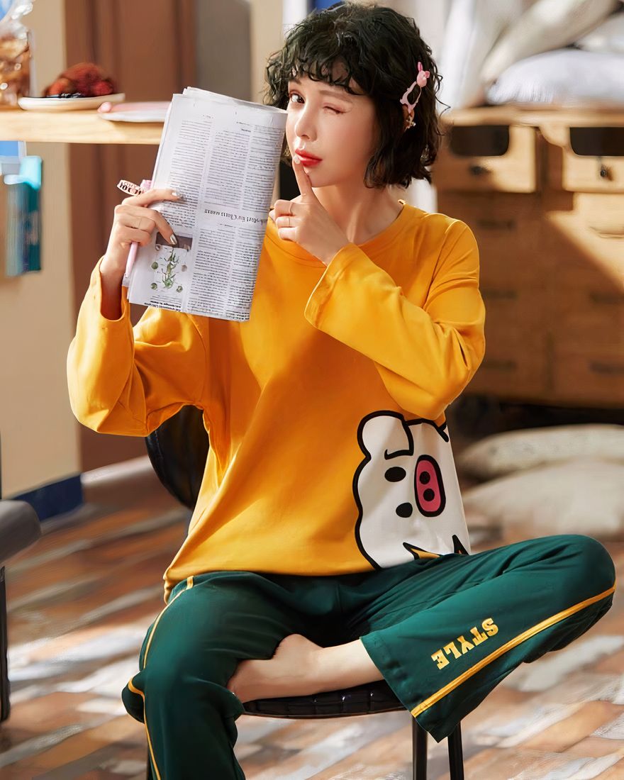 Cotton pajamas with yellow sweater and green pants worn by a woman sitting on a chair reading a newspaper in a house