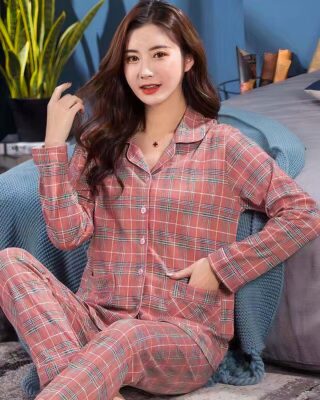 Fashionable women's two-piece check pajamas with folded collar worn by a woman sitting on a rug in front of a bed in a house