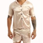 Beige satin pajamas worn by a man tattooed on his left arm, the pajamas are composed of shorts and a shirt with buttons on the front
