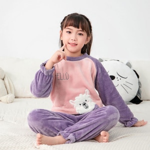 Purple children's fleece pajama set worn by a little girl sitting on a bed in a house