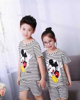 Black and white striped summer pajamas with Mickey Mousse print for child worn by a little boy and a little girl in front of a chair in a house