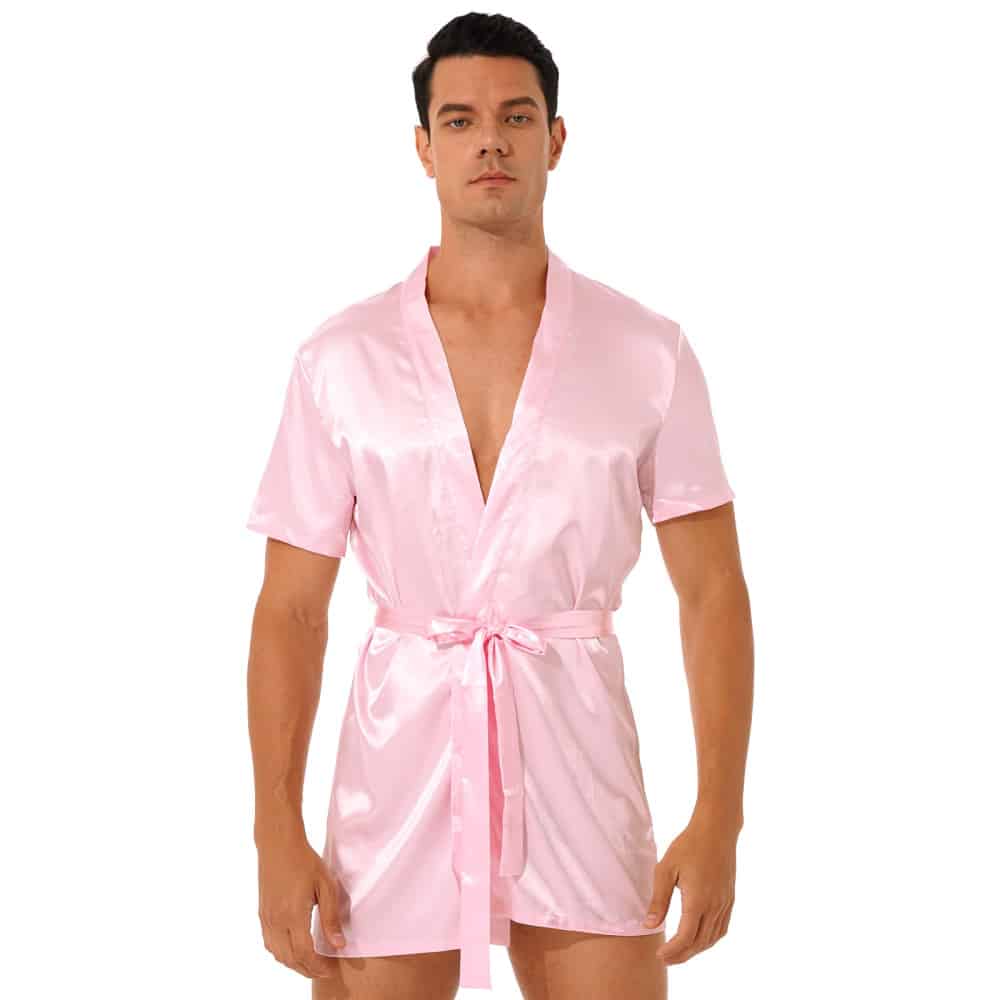 dark-haired man standing and wearing pink satin kimono pajamas tied at the waist with a belt