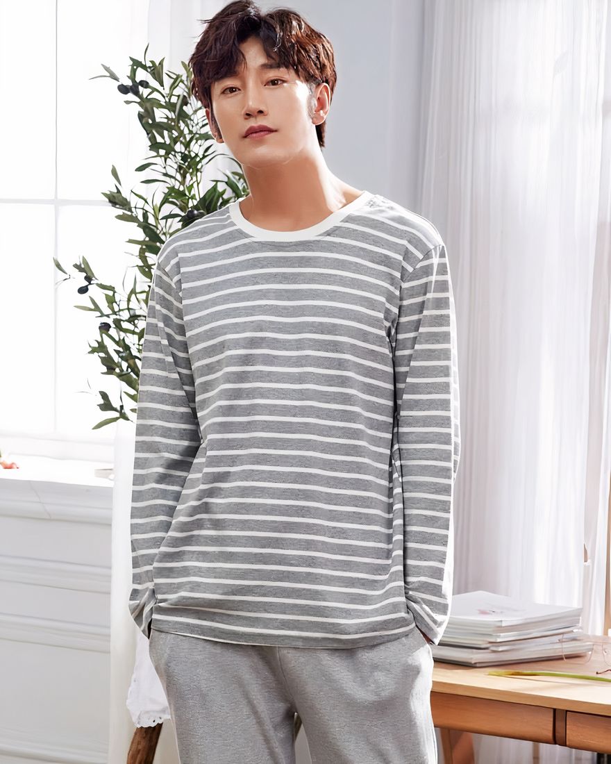 Cotton pajamas with grey striped white sweater and grey pants worn by a man in a house