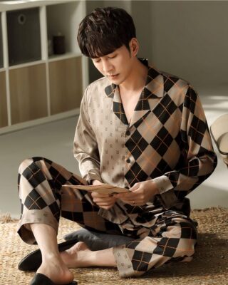 Long-sleeved cotton pajamas with folded collar worn by a man sitting on a carpet in a bedroom