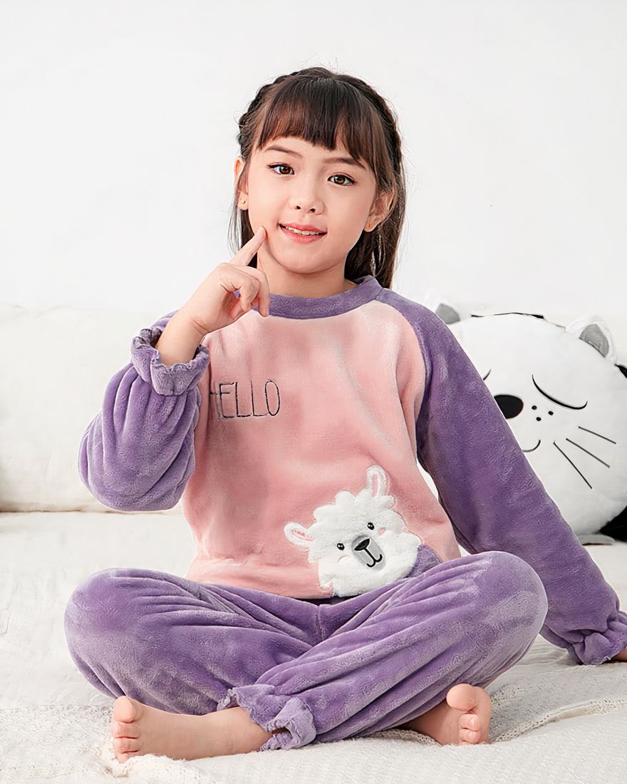 Purple children's fleece pajama set worn by a little girl sitting on a bed in a house