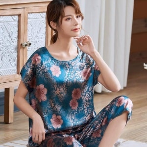 Blue short-sleeved pajamas with pink flower print worn by a woman sitting on a carpet in a house