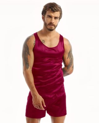 Dark-haired and tattooed man wearing black satin pajamas with a red tank top and matching red shorts