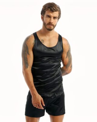 Dark-haired and tattooed man wearing black satin pajamas with a black tank top and matching black shorts