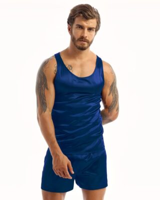 Dark-haired, tattooed man wearing black satin pajamas with dark blue tank top and matching dark blue shorts