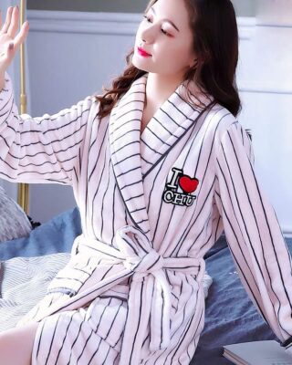 Black striped white coral fleece pajamas for women worn by a woman sitting on a bed in a house