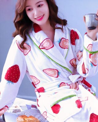 Fashionable women's strawberry fleece pajamas worn by a woman sitting on a bed in a house