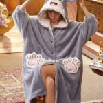 Women's grey hooded fleece pajamas with a woman wearing the pajamas sitting in a chair, with several objects