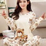 White fall pajamas with bear print for women with a woman wearing the pajamas and a gray sofa background